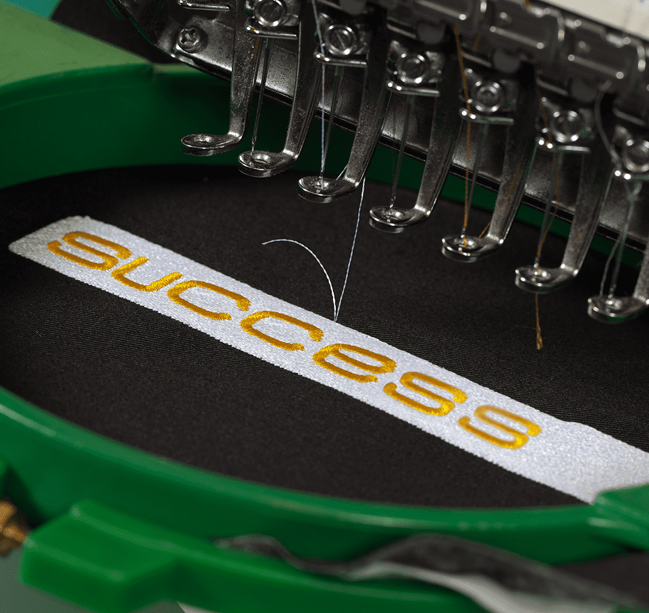 Embroidery machine stitching the word 'success' on fabric.