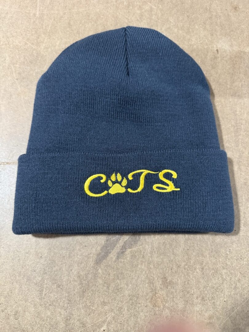 Navy blue knit beanie with yellow "CATS" and a paw print design.