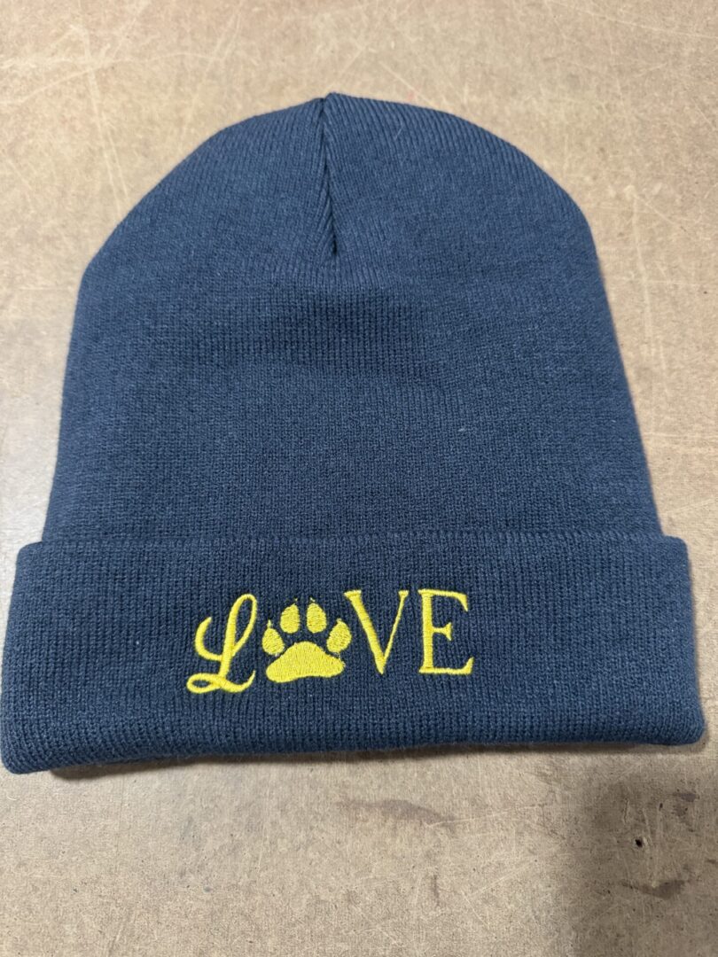 Navy blue knit beanie with the word 'LOVE' featuring a yellow paw print.