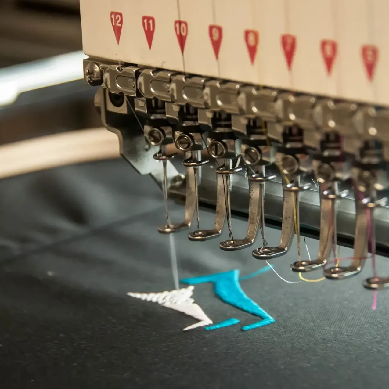 Close-up of a multi-needle embroidery machine stitching a blue and white design on black fabric.